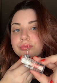 Genomskinlig läppglans i ett transparent rör med vitt lock. Applikatorn har en flexibel spets. Glansen har en mjuk rosa nyans och är applicerad på läpparna.