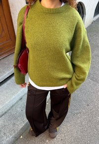 Olivengrønn strikkegenser med rund hals, kombinert med svarte treningsbukser med gule sidestriper. Brune sko og en burgunder veske.