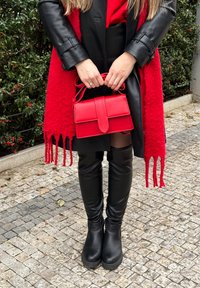 Punane käekott, millel on voltflapi disain, kantud pika punase salliga, musta nahktagi, kitsaste mustade pükste ja mustade saapadega.