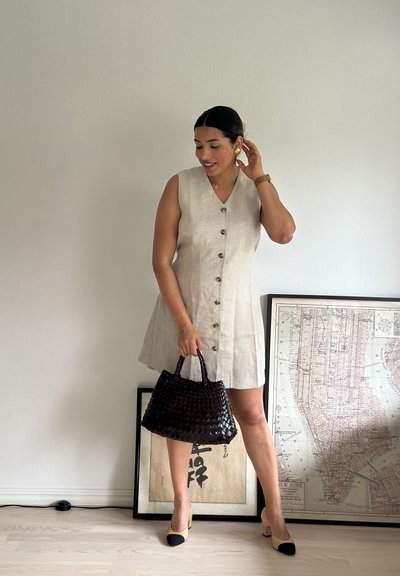 Vestido sin mangas color beige claro con botones frontales, combinado con un bolso negro de mimbre. Unos zapatos de tacón bloque en negro y beige completan el look.