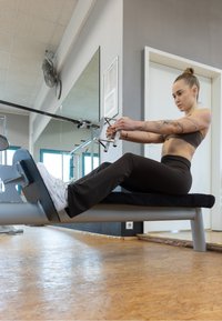 Équipement de fitness comprenant un banc rembourré, avec une personne assise tirant une poignée de câble. La scène comprend des miroirs et un sol de salle de sport.