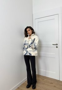 Fleecejakke med lynlås i cremefarve med blå abstrakte mønstre, med høj krave, sidelommer og løs pasform. Sorte, vidde bukser.