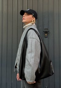 Szürke gyapjú keverék zakó magas gallérral, fekete bőr vászontáska és fekete sapka. Arany karika fülbevalók egészítik ki a modern szettet.