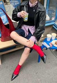 Μαύρο δερμάτινο μπουφάν πάνω από μαύρο πουκάμισο, συνδυασμένο με καρό πουκάμισο σε κόκκινο και άσπρο. Σκούρες σορτσάκια τζιν, φωτεινές κόκκινες κάλτσες μέχρι το γόνατο και μαύρες μυτερές γόβες.