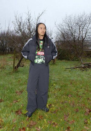 Chaqueta negra acolchada con rayas blancas, superpuesta sobre una camiseta gráfica con detalles verdes y rojos, combinada con pantalones grises anchos.