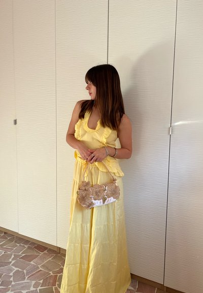 Conjunto amarillo de dos piezas con bordes rizados, que incluye un top halter y una falda larga. Un bolso con estampado floral complementa el look.