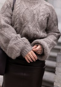 Gruby sweter pleciony w jasnoszarym kolorze z wzorami kablowymi i ściągaczami, zestawiony z dopasowaną brązową skórzaną spódnicą. Uzupełniony pierścionkiem i torebką.