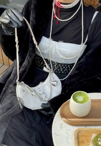 Λευκή δερμάτινη τσάντα χειρός με ασημί μεταλλικά στοιχεία, αλυσίδες και λεπτομέρειες από πέρλες. Καμπυλωτό σχήμα με διακοσμητική ραφή και μεταλλικά γούρια.