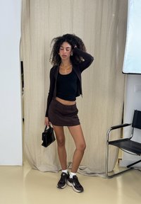 Svart kort zip-up cardigan, svart linne, brunt minikjol med randig mönster, svart handväska, vita ankelsockor och bruna sneakers.