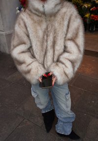 Jachetă din blană artificială, bej deschis și albă, cu guler înalt și mâneci largi. Purtați cu blugi cargo albaștri și cizme negre cu franjuri.