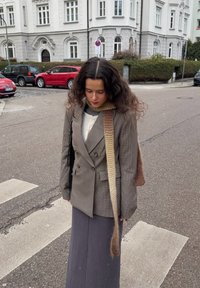 Dobbeltspent rutet blazer i grått, med en kremfarget strikkegenser og lang grå skjørt. Et strikket skjerf i beige henger ned.