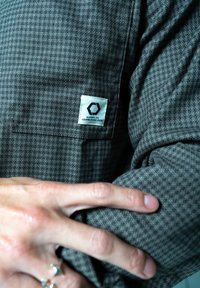 Szara koszula z długim rękawem w kratę z kieszonką na piersi z naszywką. Materiał ma miękką teksturę i subtelny wzór w kratę.