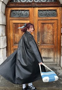 Nero cappotto in pelle con dettagli a coste sulle spalle, borsa bianca e blu, scarpe nere, calze bianche, davanti a porte doppie in legno.