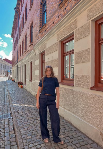 Camiseta negra de manga corta y pantalones anchos de color azul marino, combinados con un cinturón marrón. Calle de adoquines y edificios de ladrillo al fondo.