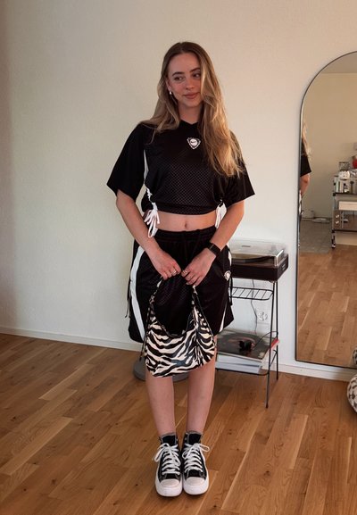 Top deportivo negro cropped con detalles en blanco, pantalones cortos negros y un bolso de estampado de cebra. Incluye características como lados con cordones y zapatillas blancas brillantes.