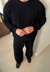 Jersey negro grueso con cuello redondo, corte relajado y textura acanalada. Combinado con pantalones negros holgados y zapatos de cuero negros.