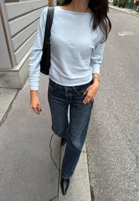 Maglione azzurro chiaro a maniche lunghe con scollatura a barca, abbinato a jeans larghi e scuri e stivaletti neri con punta. Borsa nera.