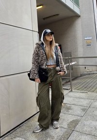 Faux karvane šunta kapuutsiga, hall lühike topp, oliivirohelised cargo-püksid ja hallid tossud. Must müts ja kott täiendavad välimust.