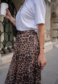 Jupe imprimé léopard en tissu doux, coupe ample, longueur mi-longue. Associée à un t-shirt blanc uni. Accessoires comprenant des bracelets dorés et du vernis à ongles.