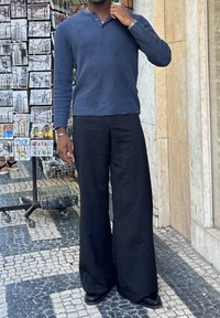 Jūras mėlynos spalvos išilgai raukšlėtas ilgomis rankovėmis henley marškinėliai, derinami su laisvais juodais kelnių. Apranga turi kasdienį fitą ir tekstūruotą, atsipalaidavusią išvaizdą.