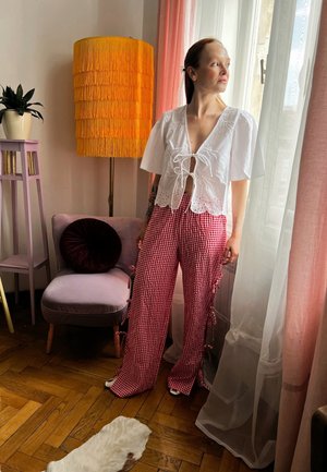 Top corto blanco con detalle de lazo y pantalones de cuadros rojos de talle alto con lazos laterales. La habitación cuenta con una lámpara amarilla con flecos y una cortina rosa.
