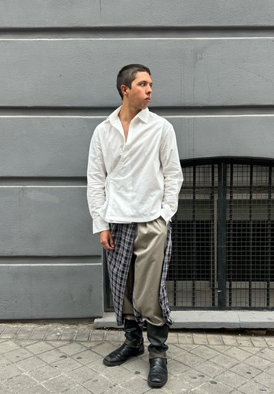 Camisa blanca con escote en V profundo, pantalones beige con un drapeado a un lado de cuadros y botines negros. Tejido texturizado, diseño en capas.