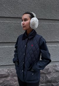 Veste matelass ée marine avec col, boutons-pression et poches latérales ; comprend des cache-oreilles blancs duveteux avec une bande texturée.