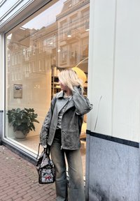 Grå läderjacka med mönstrade ärmar, kombinerad med en texturerad grå topp och byxor med vida ben. Svart väska med djärv textdetalj.