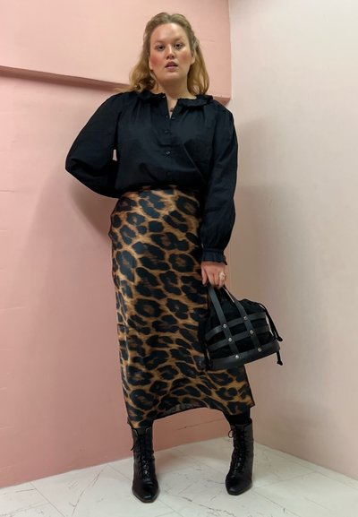 Camisa negra de botones con mangas abullonadas, combinada con una falda midi de estampado leopardo. Botas negras con cordones y un pequeño bolso negro con asas.