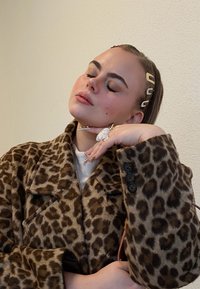 Καπαρτίνα με λεοπάρ μοτίβο φτιαγμένη από μαλακό ύφασμα, με μεγάλους γιακάδες και τρία μαύρα κουμπιά. Τα αξεσουάρ περιλαμβάνουν σφιγκτήρες μαλλιών και εντυπωσιακή τέχνη νυχιών.