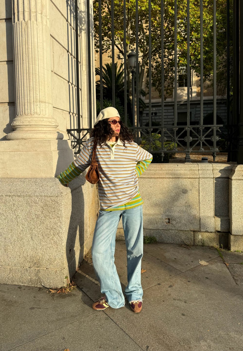 Prugaasta majica dugih rukava u bež, zelenoj i smeškoj boji, u kombinaciji s svijetloplavim širokim farmerkama i smeškim tenisicama, dodatno ukrašena beretkom i naočalama za sunce.