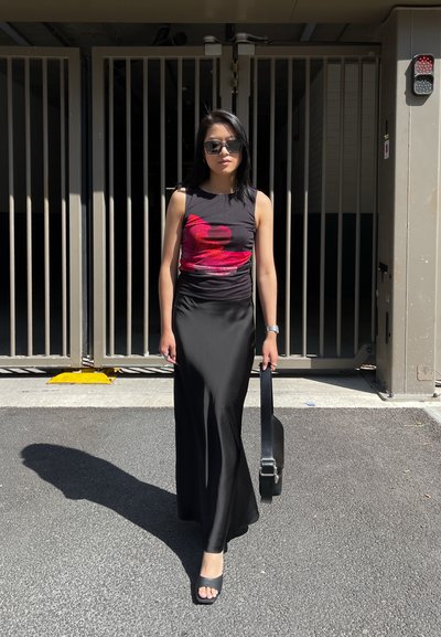 Vestido negro sin mangas con diseño gráfico rojo, textura suave y falda hasta el suelo. Los accesorios incluyen gafas de sol negras y un bolso.