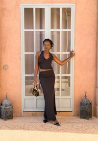 Completo nero in due pezzi composto da un top halter aderente con borchie argento e una gonna lunga arricciata. Gli accessori includono una piccola borsa nera.