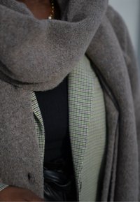 Hallhallane villane sall, mis on kihitatud rohelise ja musta ruudulise särgi peale, mille all on must top ja naha mõtteline vöö. Pehme tekstuur ja hästi kohandatud lõige.