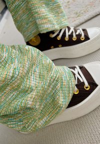 Καφέ σουέτ αθλητικά παπούτσια με λευκές καουτσούκ σόλες, χρυσά τρυπήματα και κορδόνια. Συνδυάζονται με παντελόνι από υφαντό ύφασμα σε πράσινους και πορτοκαλί τόνους.