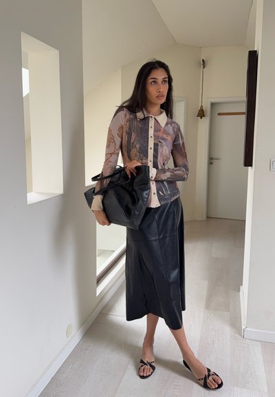 Top de manga larga con estampado en colores apagados, abotonado, con un cuello ligero; combinado con una falda negra de cuero texturizado y sandalias negras.