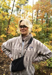 Veste en polaire avec un motif texturé de couleur marron clair, bord grise et logo. Sac en bandoulière noir au design de poche. Environnement forestier avec des couleurs d'automne.