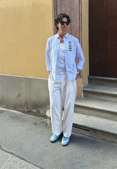 Pantalones de lino blancos, camisa de rayas verticales azul claro, camiseta blanca debajo y zapatillas azul claro. Unas gafas de sol negras completan el look.
