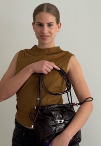 Czarna, błyszcząca torba na sznurku z srebrnymi elementami. Brązowy top bez rękawów. Torba posiada dodatkowe kolorowe akcenty na pasku.