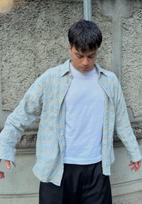 Šviesiai mėlynas, tekstūruotas marškiniai su raštuoti plaid, su mygtukais priekyje ir ilgomis rankovėmis, dėvimi ant paprastų baltų marškinėlių ir juodų kelnių.