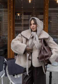 Manteau en fourrure beige textur ée avec un large col, associé à une écharpe en tricot léger. Sac en cuir marron et gants complètent le look.