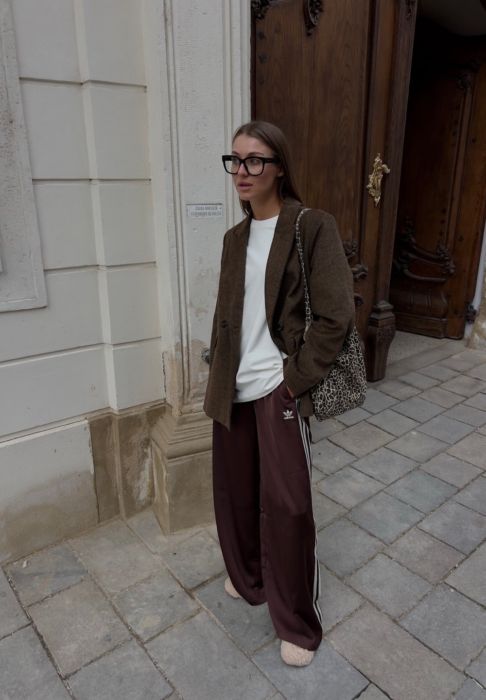 Brun texturert blazer over en hvit skjorte, burgunder joggebukser med hvite striper, briller med svart ramme, og en veske med leopardmønster.