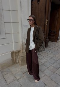 Brun texturert blazer over en hvit skjorte, burgunder joggebukser med hvite striper, briller med svart ramme, og en veske med leopardmønster.