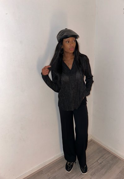 Top negro de manga larga con un sutil brillo y escote en V; combinado con pantalones negros holgados y zapatos negros con un diseño texturizado.