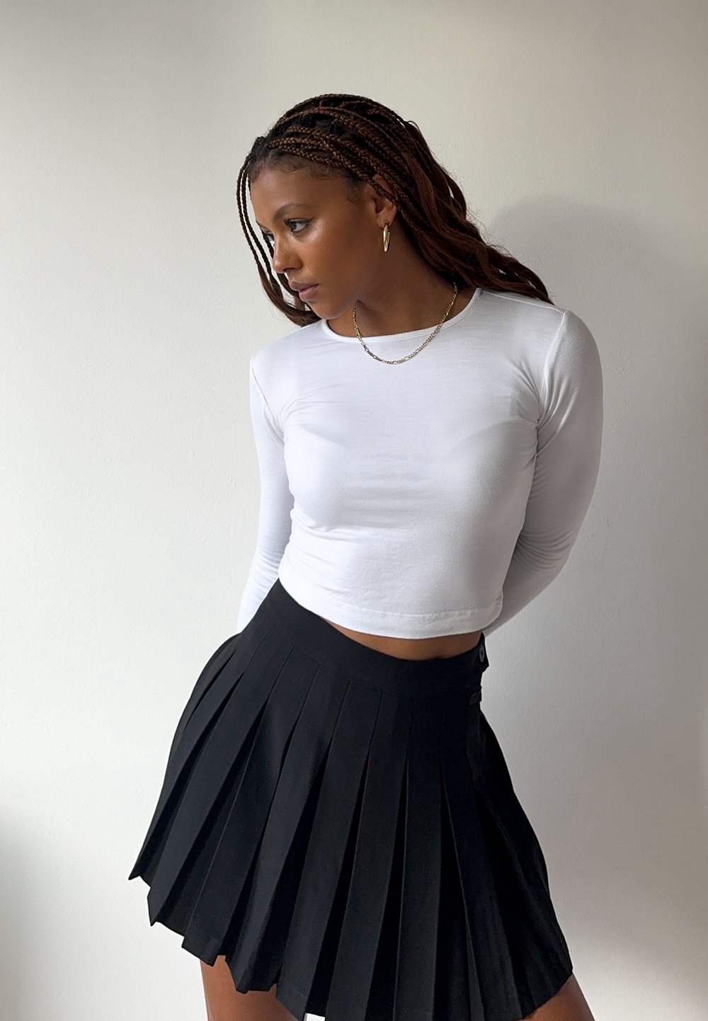 Weisses langärmliges Crop-Top, kombiniert mit einem schwarzen Faltenrock. Das Top ist glatt, während der Rock tiefe Falten und einen elastischen Bund hat.