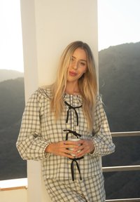 Biely prúžkovaný top s čiernymi akcentmi, s nabrúseným výstrihom, dlhými rukávmi a voľným strihom, doplnený o zladenej prúžkované nohavice.