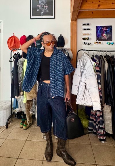 Camisa de manga corta en color marino con un diseño estampado, camiseta de tirantes negra, pantalones vaqueros amplios y cortos, botas de vaquero marrones y un bolso negro.