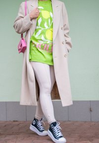 Μπεζ μακρύ παλτό, πράσιρο γραφικό t-shirt με λεμόνια, ανοιχτόχρωμα κολάν και ναυτικές ψηλές αθλητικές παπουτσές. Ορατή μικρή ροζ τσάντα.