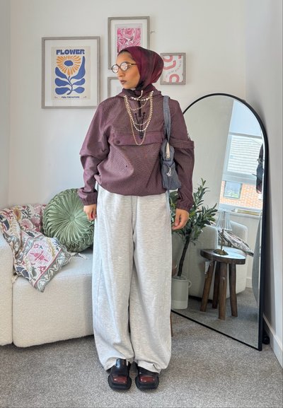 Top grande a cuadros en color burdeos, pantalones de chándal grises de pierna ancha, zapatos de plataforma negros. Los accesorios incluyen cadenas de oro en capas y un bolso estampado.