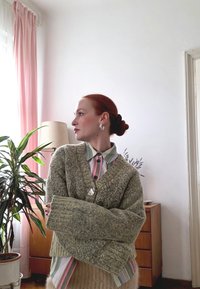 Gruby zielony dziergany kardigan z oversize'owymi rękawami i dekoltem w serek. Połączony z bluzką w paski w pastelowych kolorach z ozdobnymi guzikami.